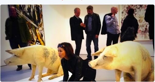 A woman kneels in a gallery between two sculptures of pigs. 