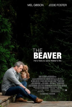 Promotional image for "The Beaver." A man sits near the woods holding a handpuppet of a beaver close to him. Caption reads "He's here to save Walter's life"