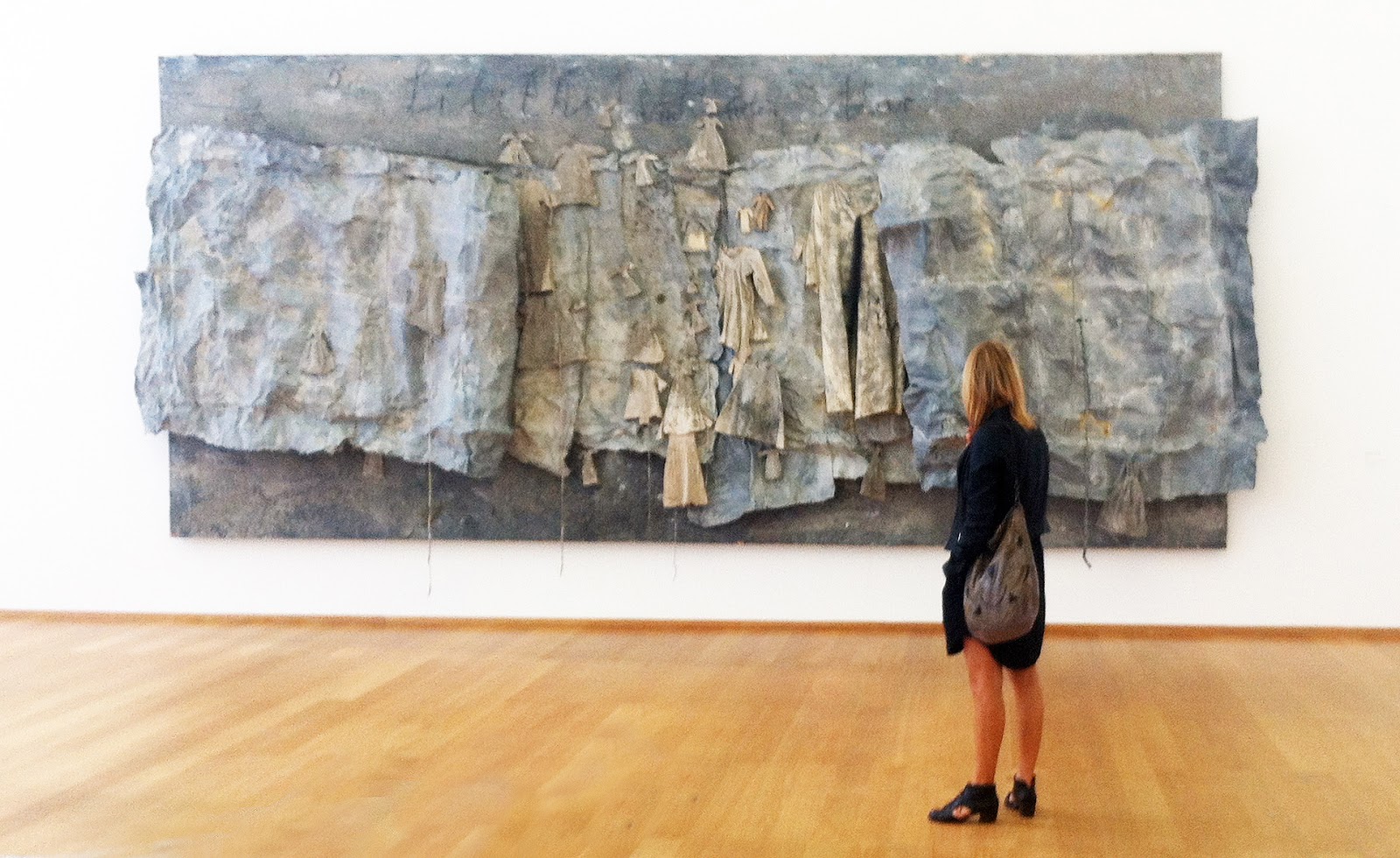 Mottled grey fabric and clothing drape across each other on a museum wall. 