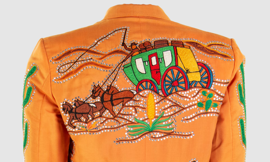 A rhinestone rusty orange jacket. A sewn on patch shows a horse drawn coach travelling through the desert.